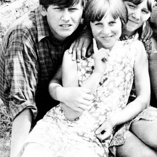Four young people pose outdoors, leaning against a tree.