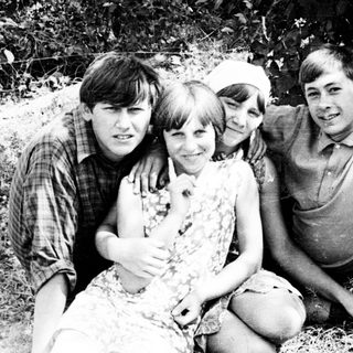 Four young people pose outdoors, leaning against a tree.