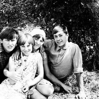 Four young people pose outdoors, leaning against a tree.