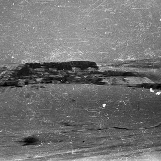 Here's a brief summary of the image: Snow-covered field with a dark, indistinct structure in the distance.