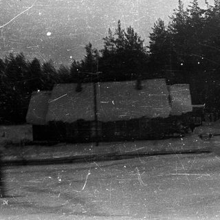 Snow-covered house with trees in a wintry landscape.