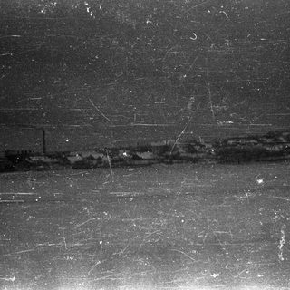 Dark, grainy image showing a blurred landscape with structures.