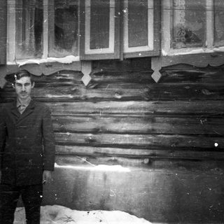 Man stands outside a log cabin, snow on the ground.