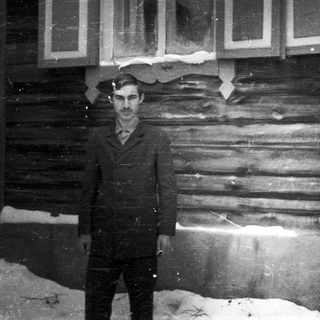Man stands outside a log cabin, snow on the ground.