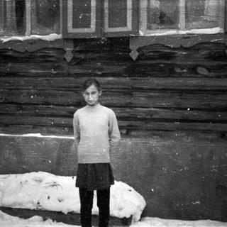 Young girl stands in front of a wooden building.
