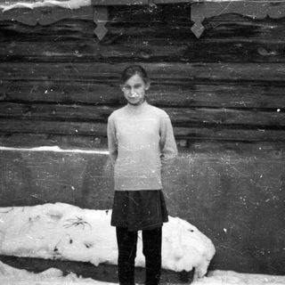 Young girl stands in front of a wooden building.
