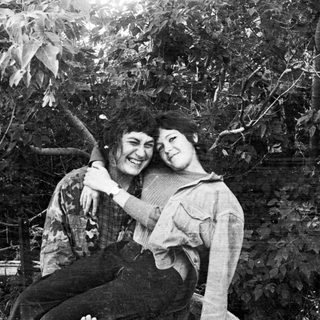 Two people sit together outdoors, smiling and relaxed.