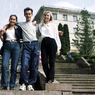 Here's a brief summary of the image: Three people stand on steps with a building in background.