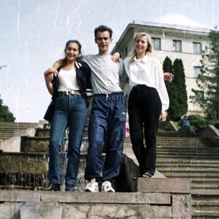 Here's a brief summary of the image: Three people stand on steps with a building in background.