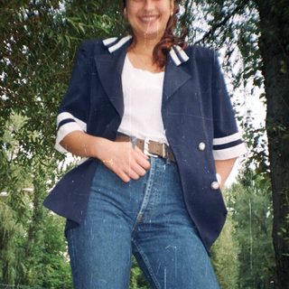 Woman stands outdoors wearing a blazer, jeans, and a white top.