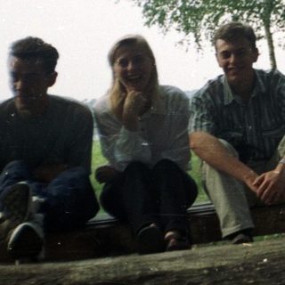 Three people sit on a log in a grassy area.