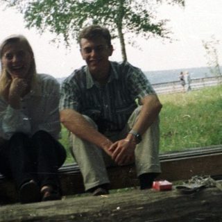 Three people sit on a log in a grassy area.
