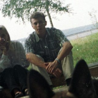Men sit on logs with a dog in a park.