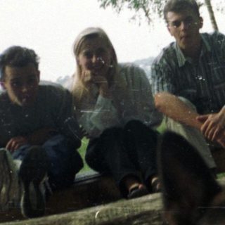 Men sit on logs with a dog in a park.
