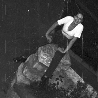 Person climbing a large, angled rock formation outdoors.