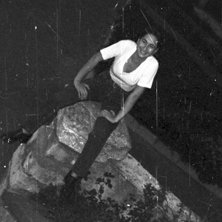 Person climbing a large, angled rock formation outdoors.