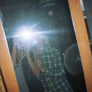Person reflected in a window, wearing a plaid shirt.