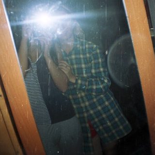 Person reflected in a window, wearing a plaid shirt.