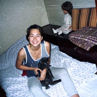 Woman sits on a bed holding a black cat.