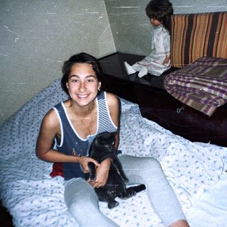 Woman sits on a bed holding a black cat.