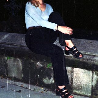 Woman sits outdoors in the rain at night.