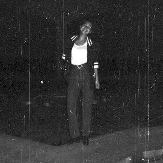 Person standing on a street at night, rain falling.