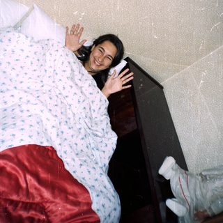 Person lying on a bed waving, teddy bear visible.