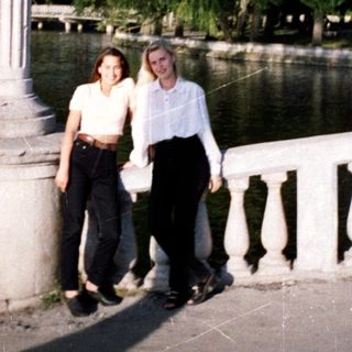 Two women stand on a stone bridge over water.