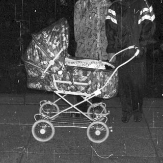 Couple stands near a stroller in a dark, rainy setting.