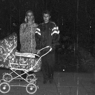 Couple stands near a stroller in a dark, rainy setting.