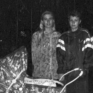 Couple stands near a stroller in a dark, rainy setting.