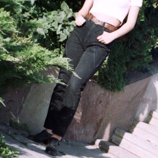Here's a brief summary: Woman sits on a concrete ledge with greenery behind.