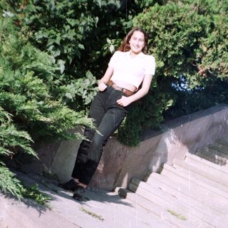 Here's a brief summary: Woman sits on a concrete ledge with greenery behind.