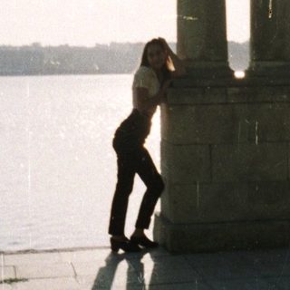 Woman stands near monument overlooking water, bathed in sunlight.
