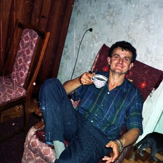 Man sits holding a cup, relaxing in an armchair.