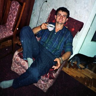 Man sits holding a cup, relaxing in an armchair.