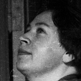 Woman in a vest looks upwards in a room.