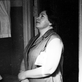 Woman in a vest looks upwards in a room.