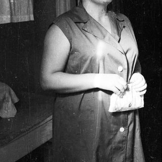 Woman in a sleeveless dress holds a clutch, looking upwards.