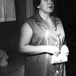 Woman in a sleeveless dress holds a clutch, looking upwards.