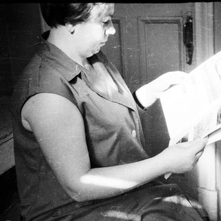 Woman reading a book, seated near a door.