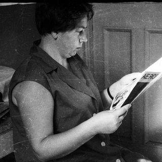 Here's a brief summary of the image: Woman reading a magazine while seated near a door.