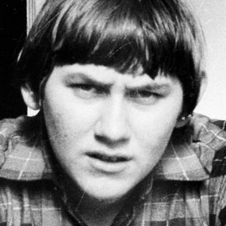 Here's a brief summary of the image: Young man in plaid shirt, looking directly at the camera.