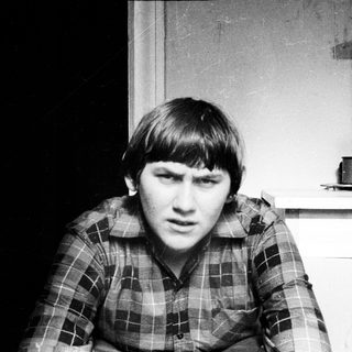 Here's a brief summary of the image: Young man in plaid shirt, looking directly at the camera.