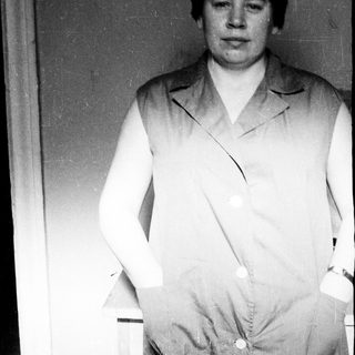 Here's a brief summary of the image: Woman in a lab coat stands near a door.