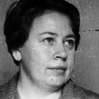 Woman in a vest stands with hands in pockets.