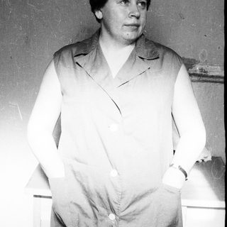 Woman in a vest stands with hands in pockets.