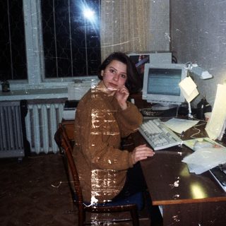 Woman sits at a vintage computer desk in a room.