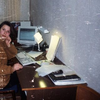 Woman sits at a vintage computer desk in a room.