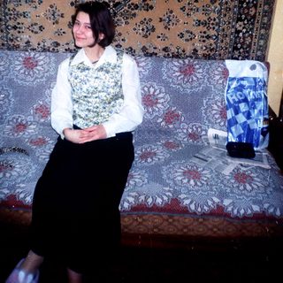 Woman sits on a patterned couch with a portrait above.